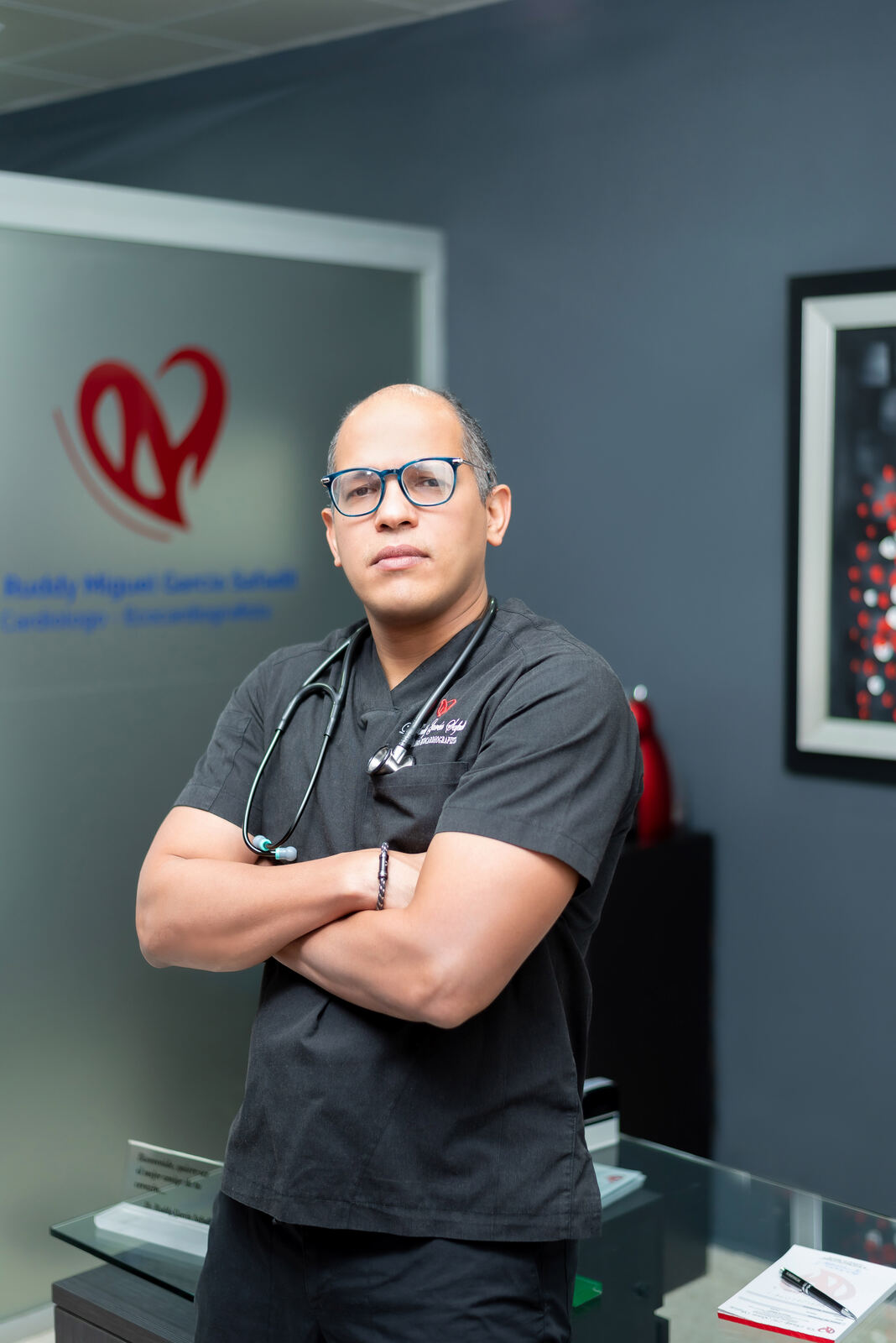 El Dr. Ruddy Garcia Safadit con uniforme quirúrgico y estetoscopio en su consultorio
